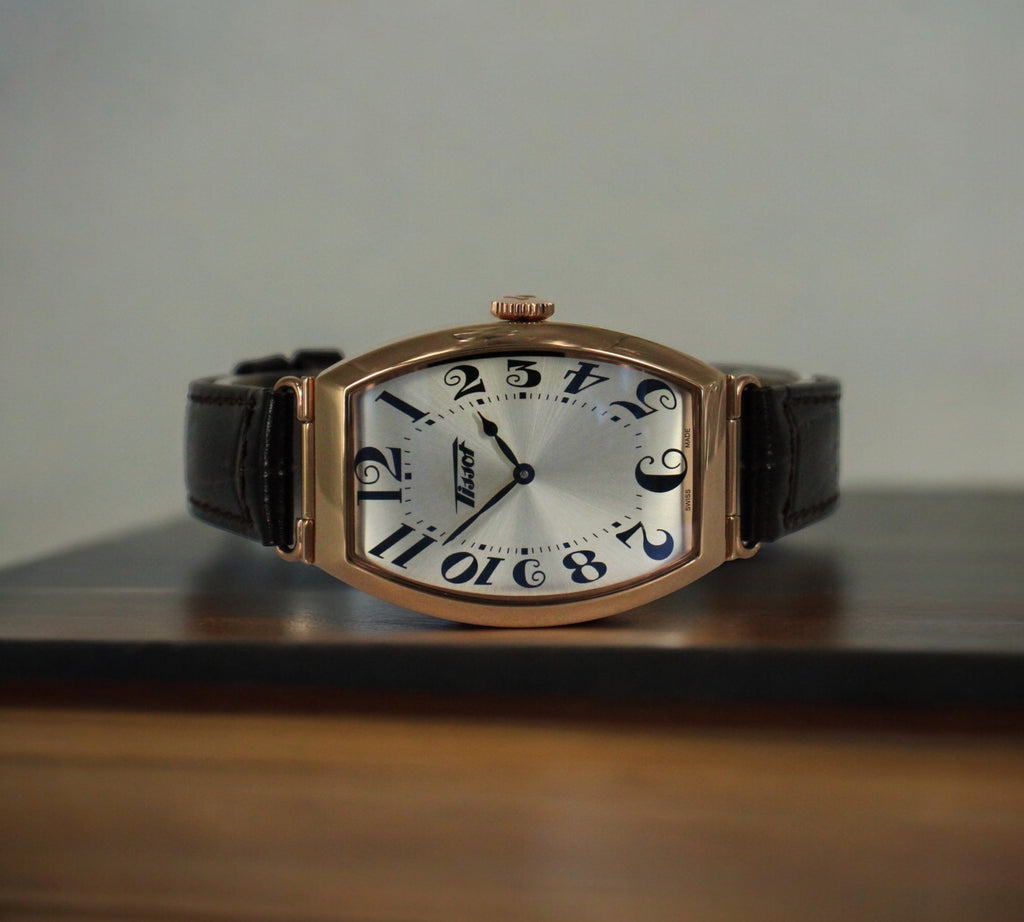  Elegante Tissot Heritage Porto: roségouden kast, zilveren wijzerplaat, bruine leren band, tijdloze stijl, Swiss Made. Verkrijgbaar bij Optiwatch.